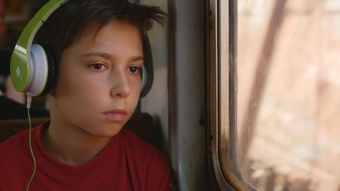 The boy in the headphones looks sad out the window of the train