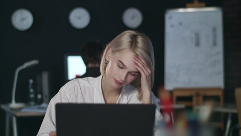 Upset business woman looking at laptop computer in night office. Unhappy businesswoman reading bad statistics data. Young woman analyzing unsuccessful business results