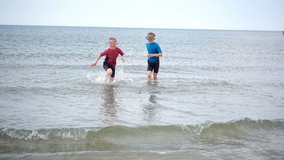 Slow-motion video of two happy children in neoprene swimsuits running on the beach and playing with waves and sand