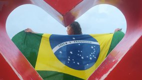 Happy girl with Brazil flag fluttering on her back. Smiling inside a heart on a landmark in Natal city, Rio Grande do Norte, Brazil. - Powered by Shutterstock - Get 15% off with code: PIKWIZARD15