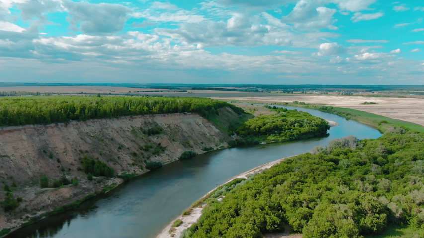 Beautiful aerial 4k view over the curving river along the fields and forest