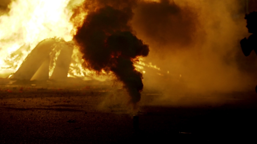 Black silhouettes of kids playing outdoors in the smoke. Big fire during the celebration of Saint Joan holiday in Barcelona. Big flames in the evening. Fireworks. Burning rest overs of used furniture