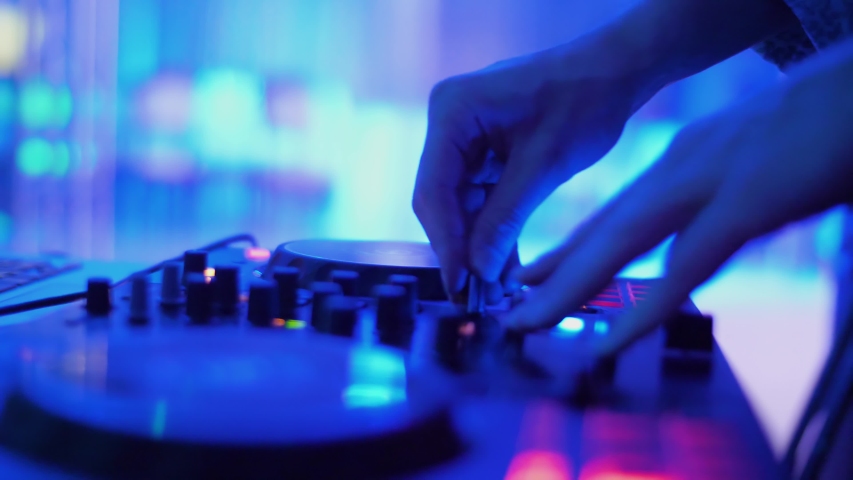 DJ sound control console for mixing dance music and laptop in disco club. Hands touching buttons sliders, playing electronic music on mixing deck, color illumination in nightclub dance party. Close up Royalty-Free Stock Footage #1032437960