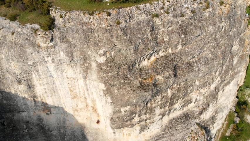 Aerial view of strong woman rock climbing, extreme vertical wall climb. Rock climbing dangerous mountain, active sport summer activity. Female climber, climbing gear