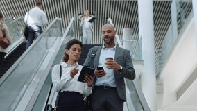 business woman using tablet computer discussing work with businessman colleague showing ideas corporate executives on escalator in office lobby 4k - Powered by Shutterstock - Get 15% off with code: PIKWIZARD15