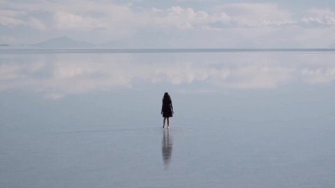 Woman walks on the vastity of the salt flats of Bolivia, rain season and water reflex. Slow motion. Desolation on nature