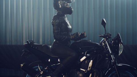 Stylish brutal biker girl in a black glossy helmet and black leather jacket is sitting on his bike. Neon illumination. Cooking in the night races. Moto service. Frame for the film.