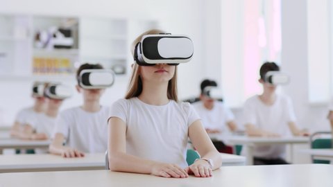 Excited preteen students using augemnted reality for studying in modern school. View of pupils with VR headsets during a computer science class.