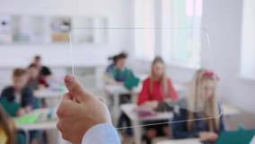 Smart innovative teacher and his students using digital tablet computers during a lesson. Close-up of man holding and swiping on a transparent modern tablet in the classroom. Futuristic study process. - Powered by Shutterstock - Get 15% off with code: PIKWIZARD15