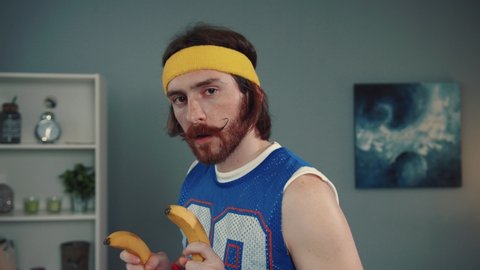 Portrait of seductive handsome young retro sportsman using bananas instead of guns blowing dust off the handgun training in his living room at home.