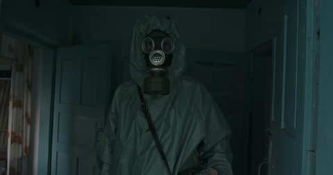 Man in Vintage WWII Hazmat suit and gas mask standing in the doorway of a house. The dosimeter in the Chernobyl zone checks the state of the buildings and the level of radiation pollution. RAW video - Βίντεο στοκ