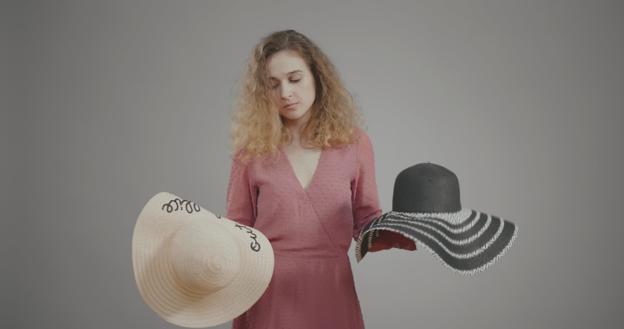 Young woman chooses between two hats, looks attentively at one, then at another, picks one and puts on head, adjusts it and looks closely at it. Choice, indecisive and hesitant Royalty-Free Stock Footage #1032476783