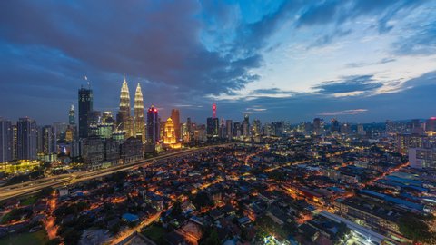Time lapse: Aerial cityscape view during dusk overlooking Kuala Lumpur city skyline at sunset from day to night with busy city streets in Malaysia.