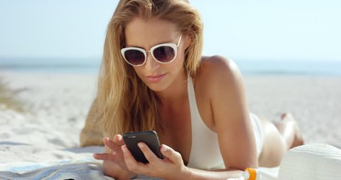 beautiful woman using phone text messaging conversation lying on beach suntanning RED EPIC DRAGON