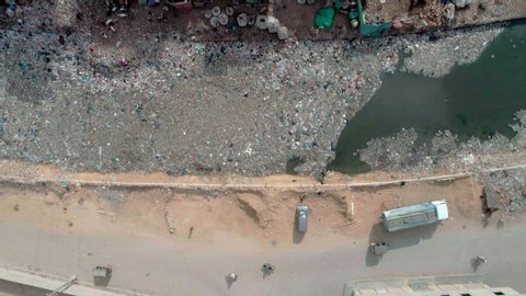 Drone over a polluted slum area in Karachi, Pakistan. Next to broken, dilapidated homes is a river strewn with garbage and overflowing with sewage.