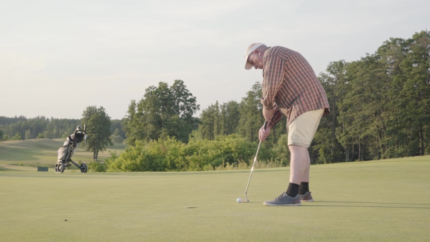 Mature man playing golf alone on the golf field. Senior man hit the ball using golf club. The guy makes a punch and kicks the ball. Summer leisure. Victory concept
