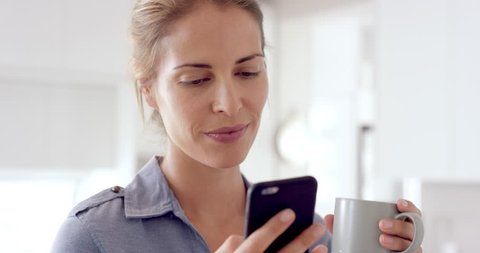 Real woman using mobile phone at home drinking coffee enjoying relaxing lifestyle