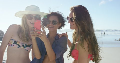 Group of beautiful girl friends taking selfies on the beach on summer vacation using pink phone RED DRAGON