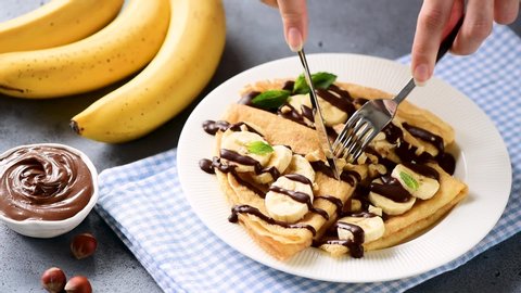 Person eating crepes stuffed with banana and chocolate spread. Tasty breakfast sweet food