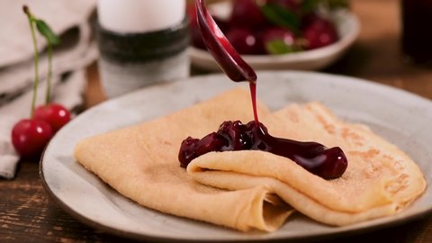 Person adding sweet cherry jam to breakfast crepes or pancakes, slow motion