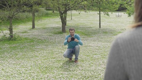 Photographer taking photos of young woman standing in front of a pond in a park. Shot on 4K.