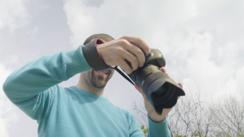Photographer taking photos of young woman lying in grass taking selfies on phone in a park with a pond. Shot in 4K.