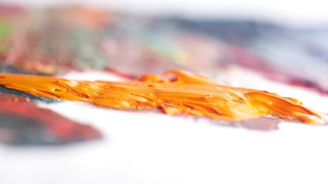 Close-up of large white brush smearing the orange oil paint on the painted canvas. Action. Arts and painting concepts