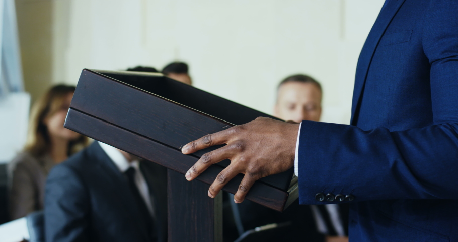 Close up of the African American male hands laying on the podium while man having a business speech to the audience during congress.