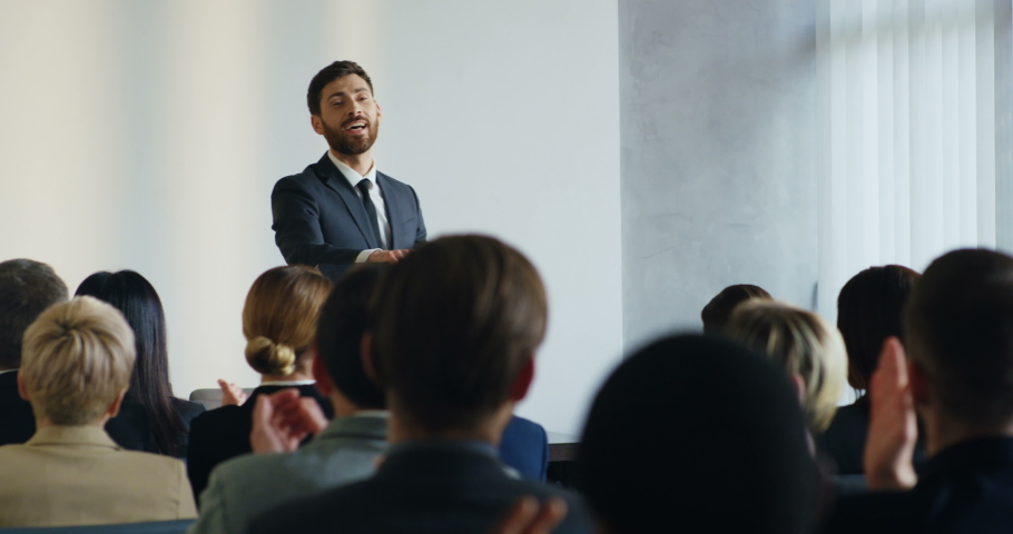 Caucasian handsome youg business coach having his speech at the conference and pointing at someone from the audience, then coming closer to that woman.