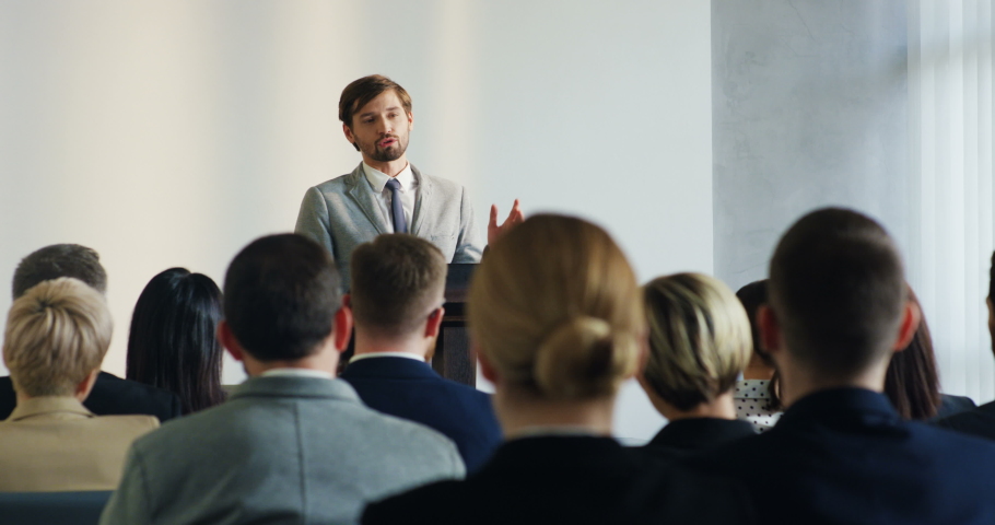 Male Caucasian business lector talking and coaching big group of people who sitting and studing at the conference.