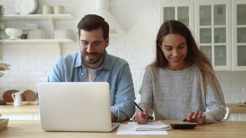 Happy young husband and wife using calculator laptop computer talking doing paperwork together sit at kitchen table discussing family mortgage loan payments pay bills manage finances expenses at home | Shutterstock HD Video #1032517241