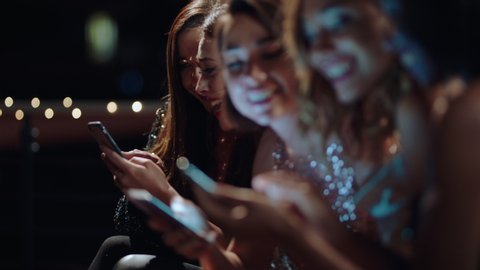 beautiful group of women using smartphones chatting sharing glamorous party event on social media girlfriends having fun evening wearing gorgeous fashion hanging out on rooftop at night
