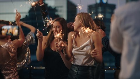 beautiful young women dancing with sparklers girl friends celebrating new years eve at glamorous party wearing stylish fashion friend using smartphone sharing video of celebration on social media