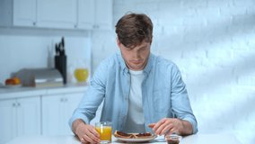 man eating bread toasts with jam, drinking orange juice, looking around and smiling in kitchen