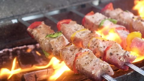 Pork delicious shish kabobs pierced with skewer. Meat with red, yellow, green pepper, sprinkled spices. fried on an open fire on a charcoal grill in tongues of bright hot flame. from food goes steam.