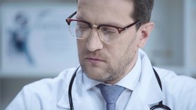 confident doctor in glasses holding pill and looking at camera