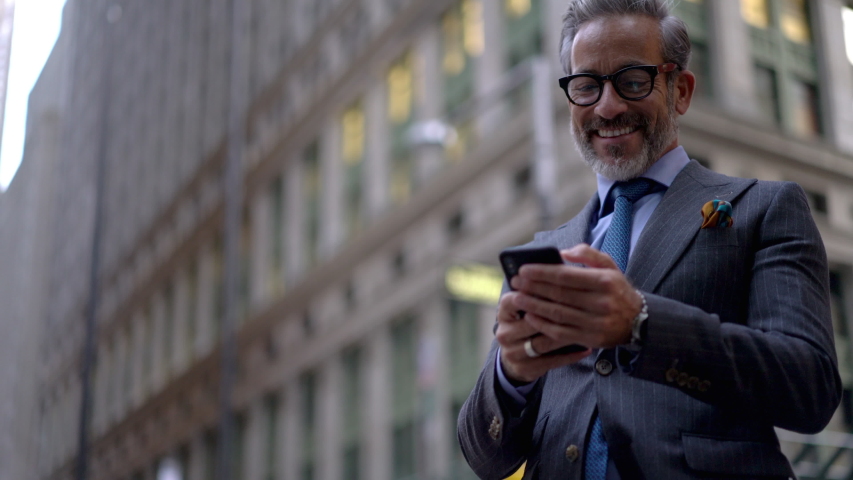 Cheerful executive manager in formal wear reading notification with business proposal on smartphone standing near at urban setting, excited entrepreneur typing sms message on cellphone on street 