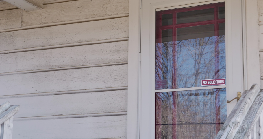 Man knocking on a front door tries to look inside the house to see if anyone is home