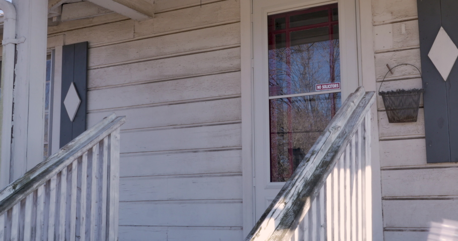 Man walks up to a front door of a house and knocks on the door holding a notebook as if he is taking a survey, volunteering for a political campaign, or running a census
