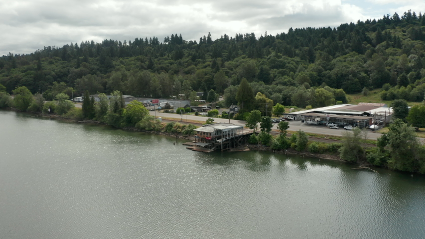 aerial orbit around abandoned boat house with traffic behind on a cloudy day.