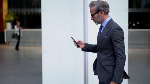 Slow motion effect, Caucasian businessman dressed in formal suit browsing network website using modern smartphone gadget. Middle aged man using mobile phone outdoors in city