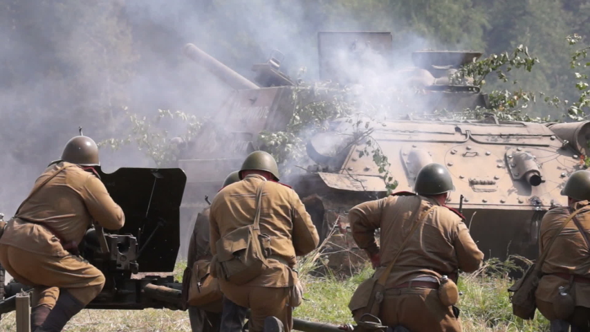 War. Infantrymen hiding behind the tank go on the attack on the enemy and shoot a weapon.