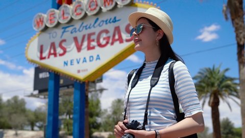 Happy young asian woman visitor standing near Las Vegas Welcome sign. Beautiful girl travel photographer smiling with Las Vegas billboard on background. female tourist with camera trip in Nevada USA