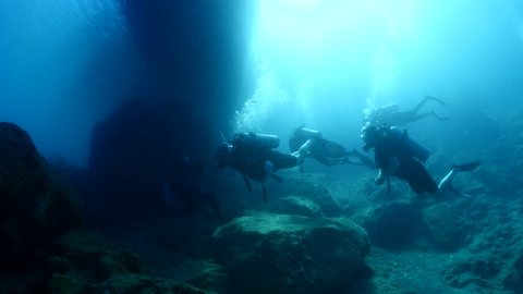 scuba divers exploring underwater with sun beams sun rays and sun shine underwater rocky ocean scenery