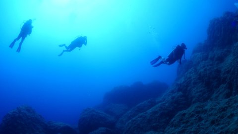 scuba divers diving underwater with sun beams sun rays and sun shine underwater rocky ocean scenery landscape 
