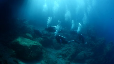 scuba divers diving underwater with sun beams sun rays and sun shine underwater rocky ocean landscape scenery with ait bubbles