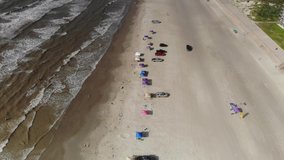 Angled view of the ocean and beach with no skyline, Moving towards the water over several tents and cars. Aerial footage of the North Packery Channel Jetty in Corpus Christi TX