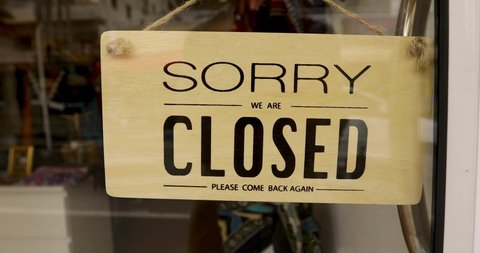 Inscription Sorry closed on wooden banner hanging on glass door in shop