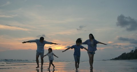 Silhouetted happy asian family playing and having fun on the beach at sunset. Slow Motion. Family, Freedom and Travel concept.
