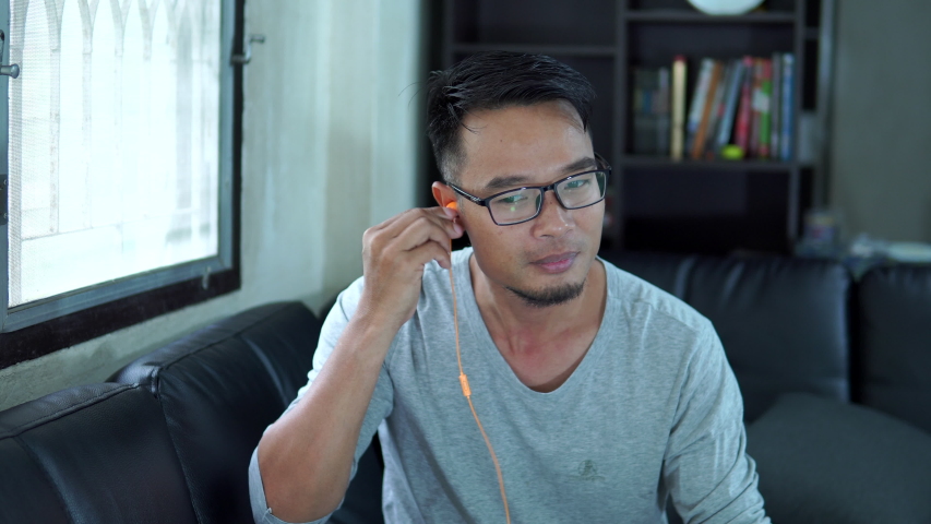 Asia man listening music by earphone in the living room | Shutterstock HD Video #1032592883